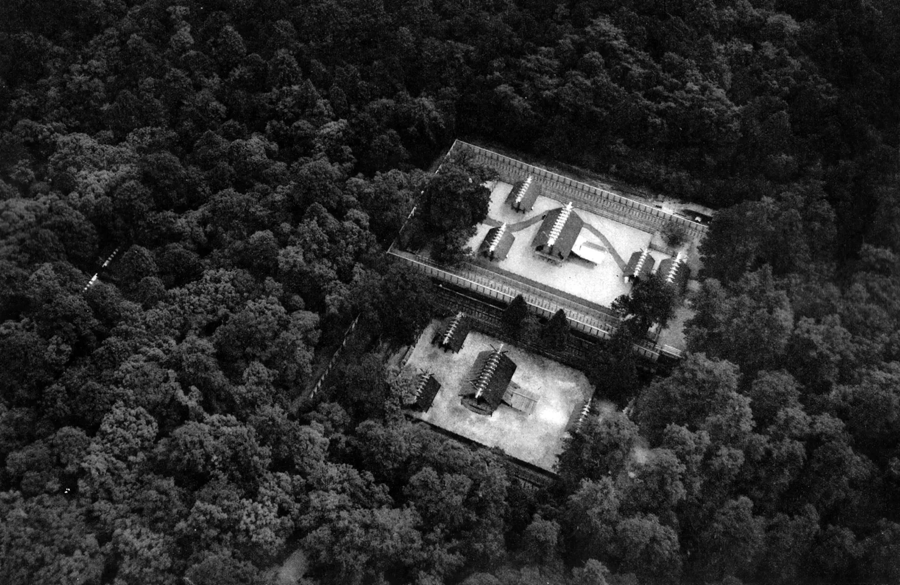 A black and white aerial photograph of two walled rectangular compounds of wooden shrine buildings side by side in a dense forest