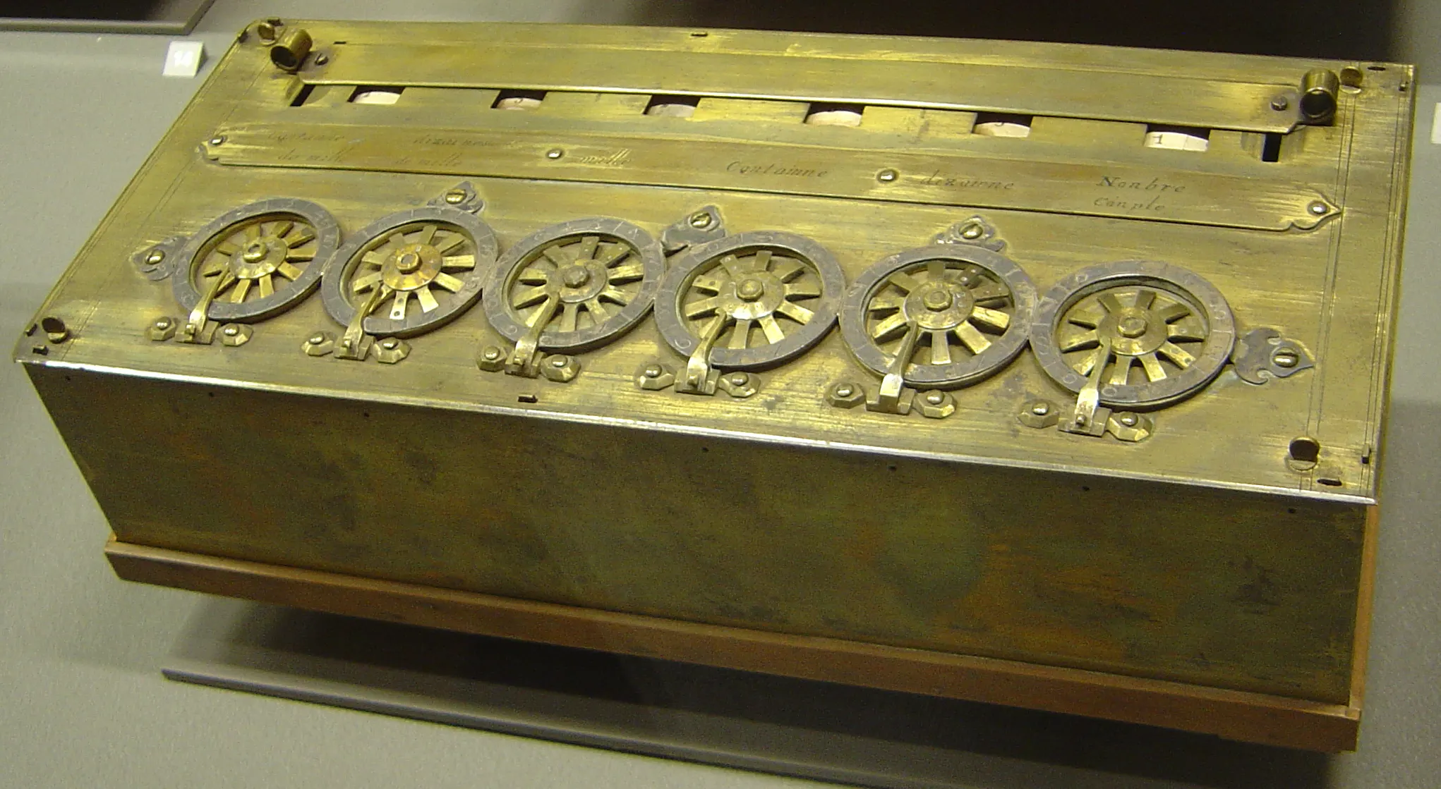 A brass box with a row of six spoked dials along its front and small result windows along the top edge